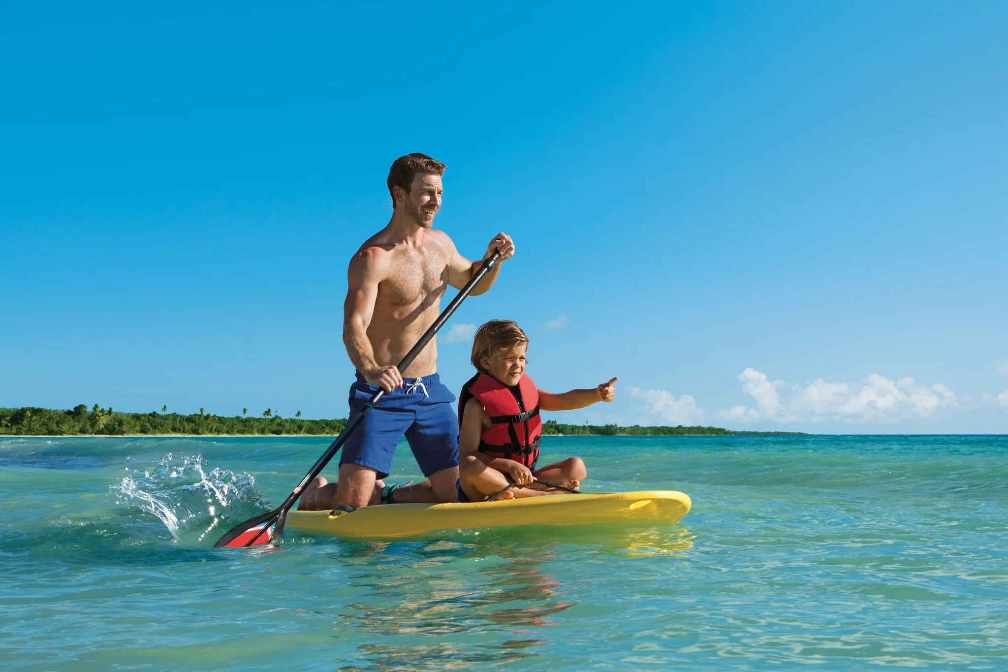 Father and son paddleboarding together in the Caribbean Sea at Dreams Dominicus La Romana Resort.