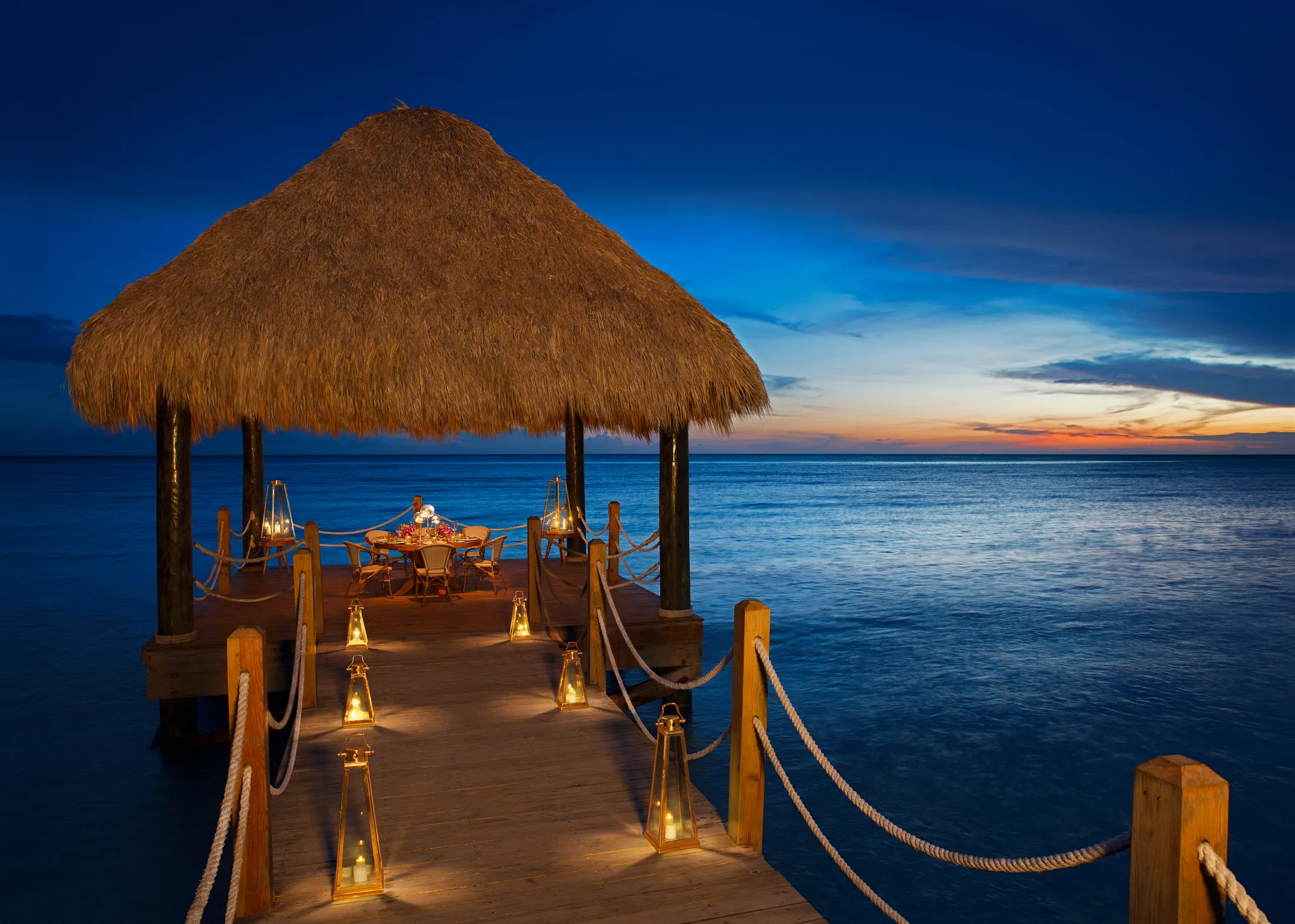 Romantic candlelit dinner on a private ocean pier at Dreams Dominicus La Romana Resort during sunset in Bayahibe.
